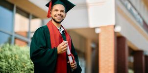 Junger Mann mit schwarzer Uni-Robe und Diplom in der Hand lacht in die Kamera