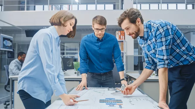 Eine Gruppe von Ingenieuren diskutiert an einem Tisch stehend über einem Bauplan